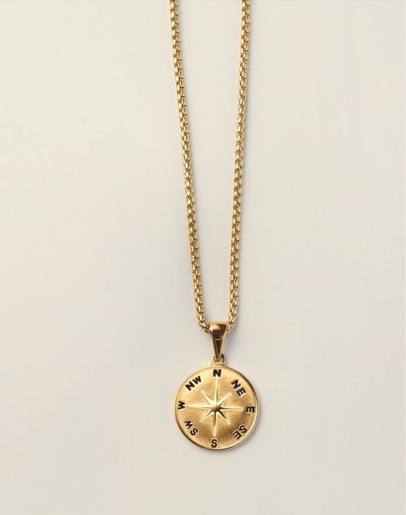 Close-up of gold-tone compass rose pendant showing engraved directional points on box chain
